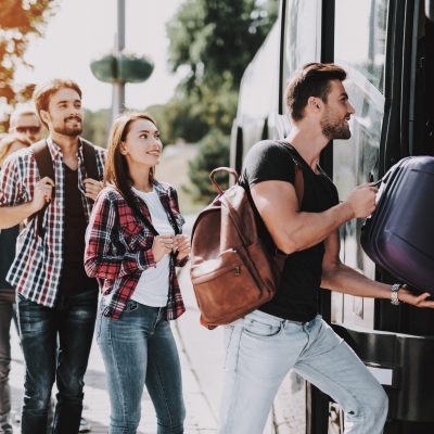 Group of Young People Boarding on Travel Bus. Happy Travelers Standing in Queue Holding Luggage Waiting their turn to Enter Bus. Traveling, Tourism and People Concept. Summer Vacation